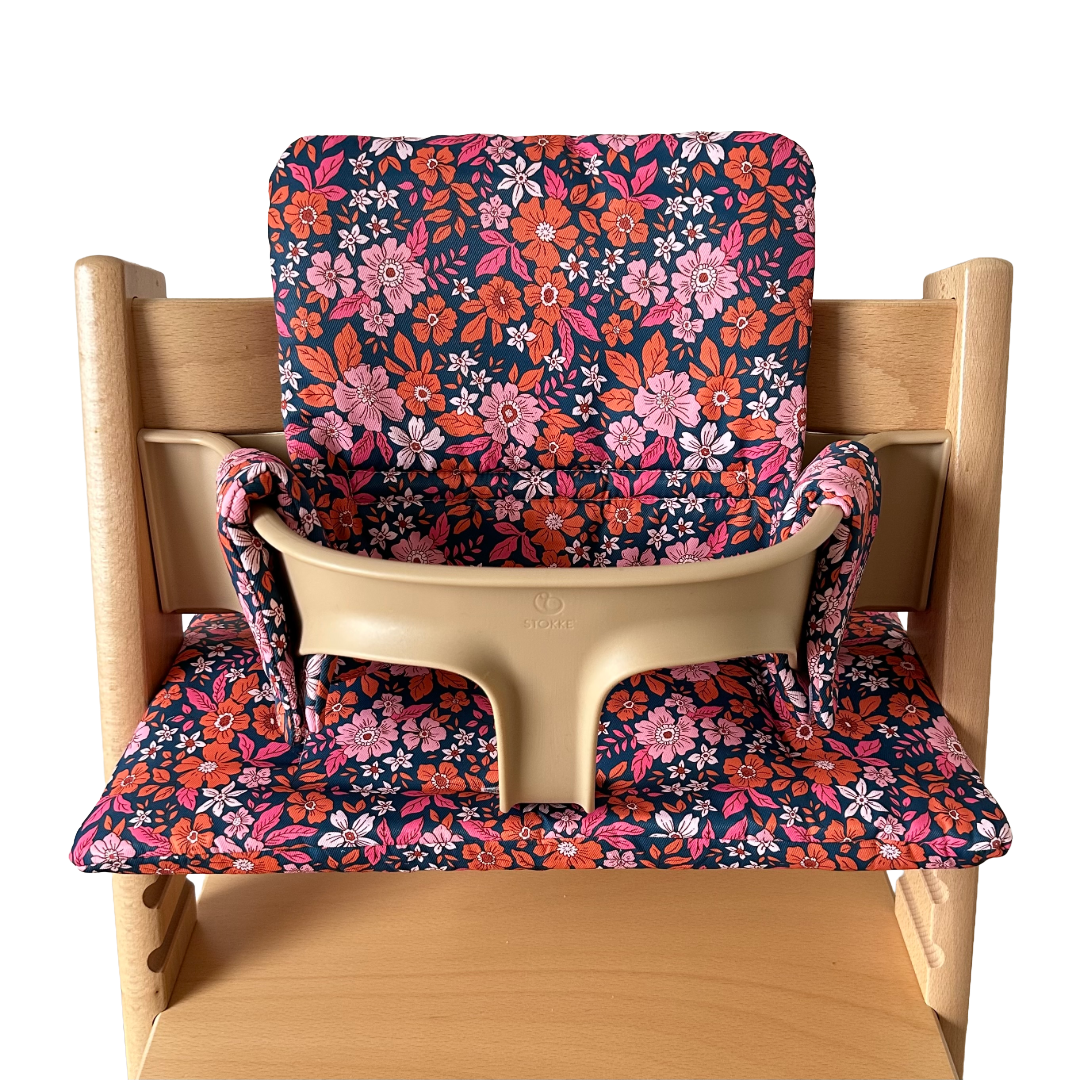 Kussenset voor Stokke Tripp Trapp met bloemenprint (oranje, roze). Vooraanzicht van het kussen op de stoel met gebruik van de babyset.