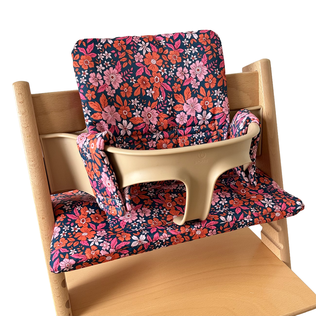 Kussenset voor Stokke Tripp Trapp met bloemenprint (oranje, roze). Zijaanzicht van het kussen op de stoel met gebruik van de babyset.
