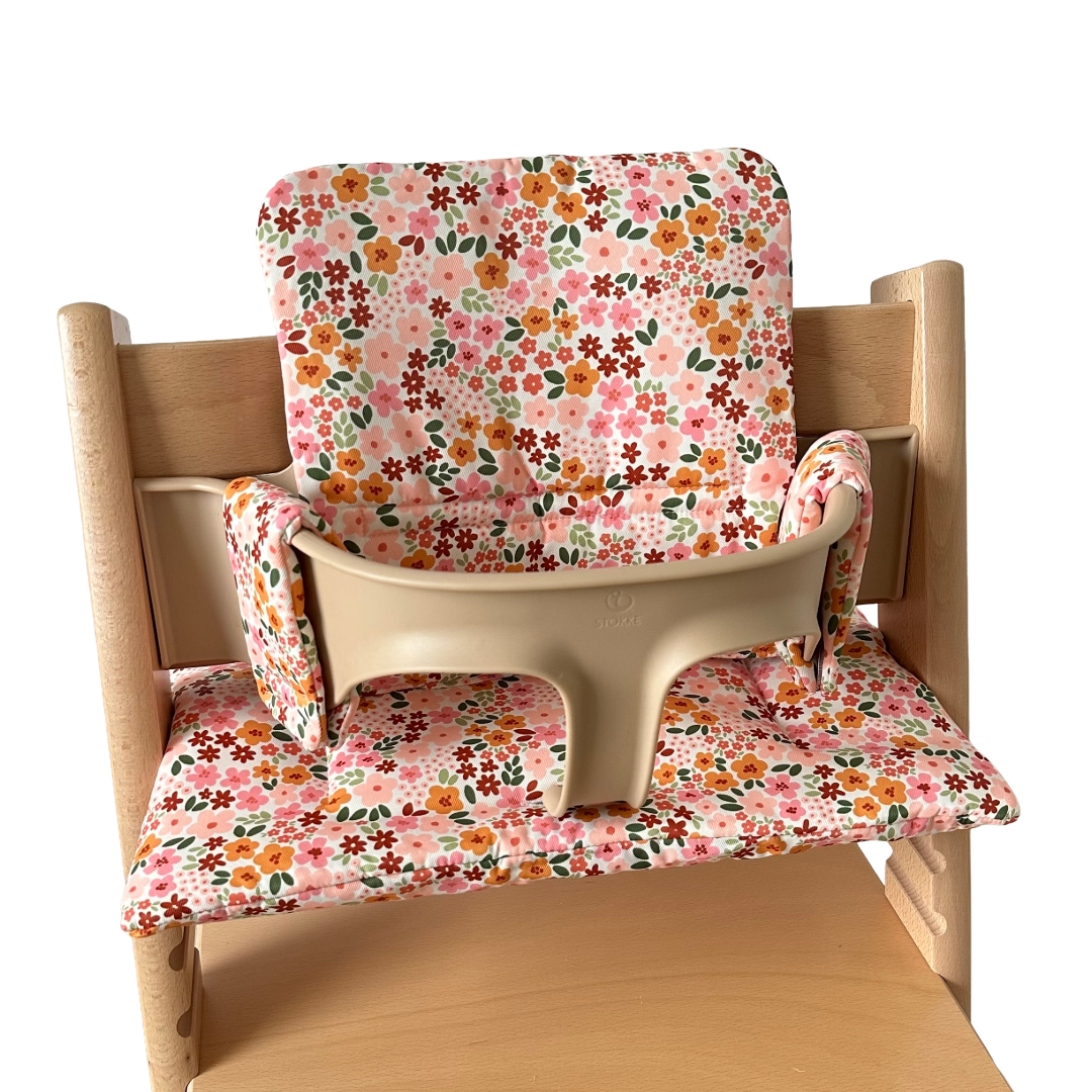 Kussenset voor Stokke Tripp Trapp met herfstbloemen (oranje, rood, roze). Zijaanzicht van het kussen op de stoel met gebruik van de babyset.