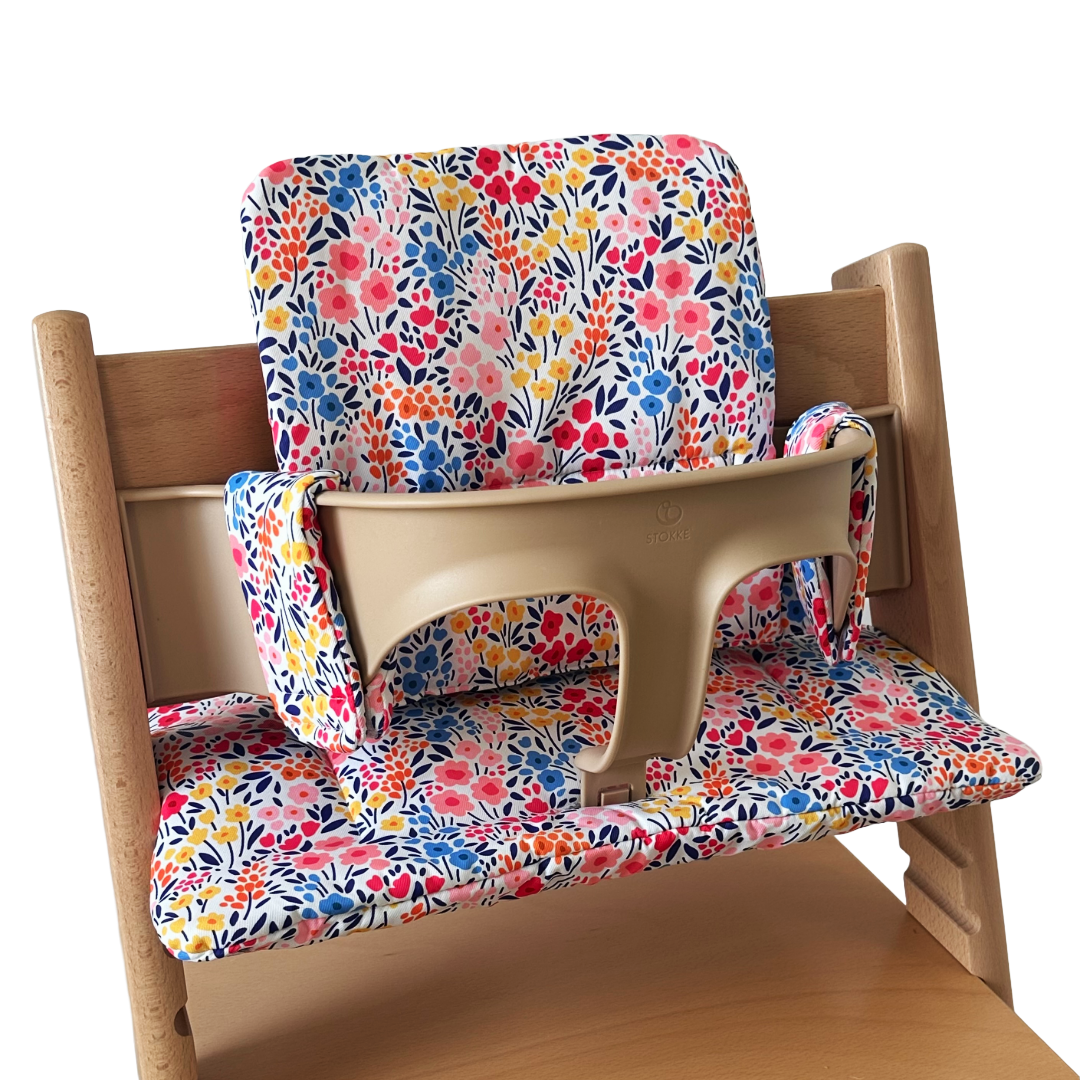 Kussenset voor Stokke Tripp Trapp met kleurrijke bloemen. Zijaanzicht van het kussen op de stoel met gebruik van de babyset.