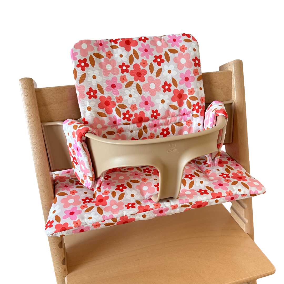 Kussenset voor Stokke Tripp Trapp met print madeliefjes (roze, rood, wit). Zijaanzicht van het kussen op de stoel met gebruik van de babyset.