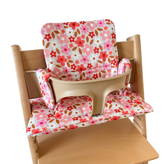 Kussenset voor Stokke Tripp Trapp met print madeliefjes (roze, rood, wit). Zijaanzicht van het kussen op de stoel met gebruik van de babyset.